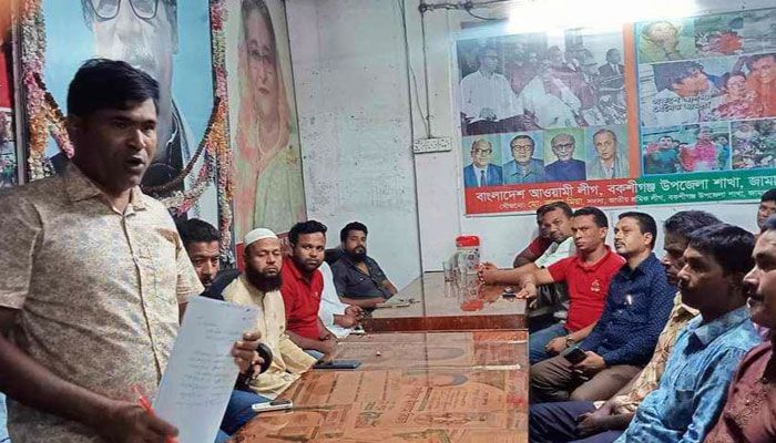 ছবির বাঁ পাশে কাগজ হাতে দাঁড়িয়ে রয়েছেন আসামি শামীম খন্দকার ও ডানে (লাল গেঞ্জি) বসে আছেন অপর আসামি ইসমাঈল হোসেন স্বপন মণ্ডল।