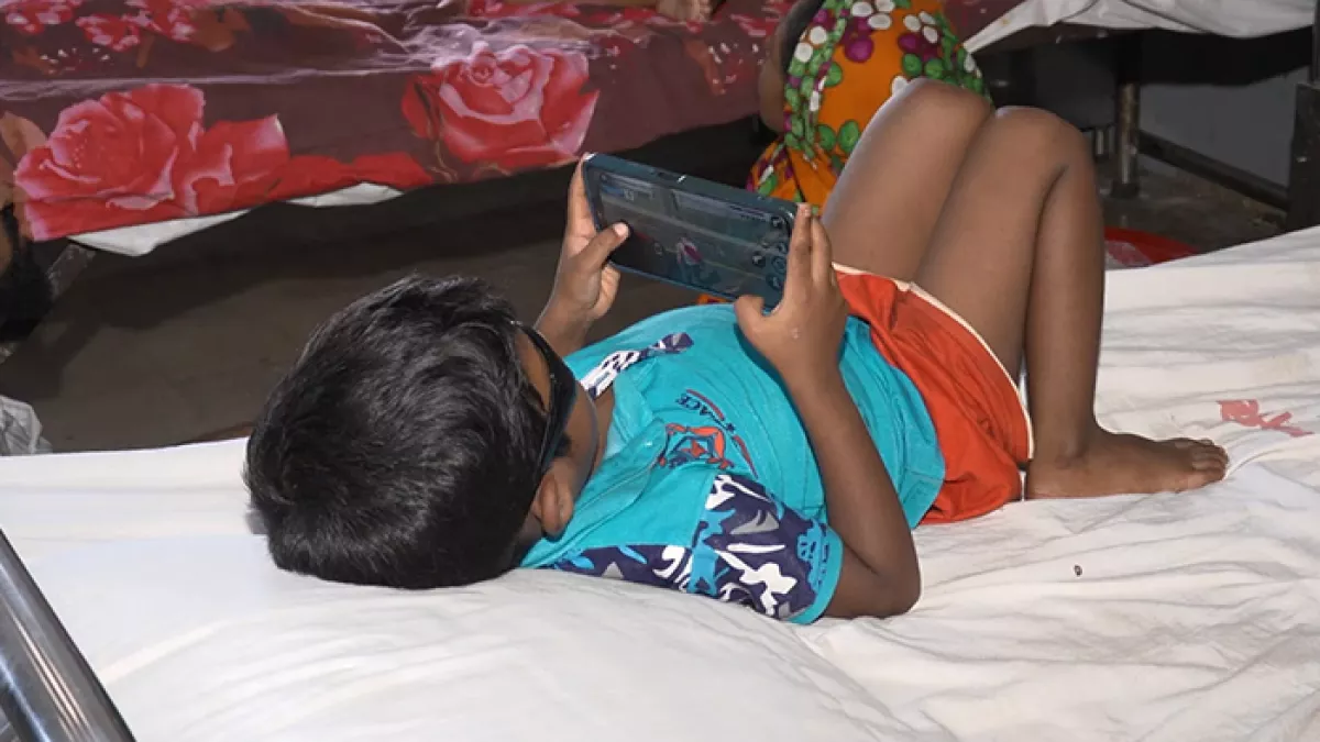 বিছানায় শুয়ে স্মার্টফোনে গেম খেলছে একটি শিশু